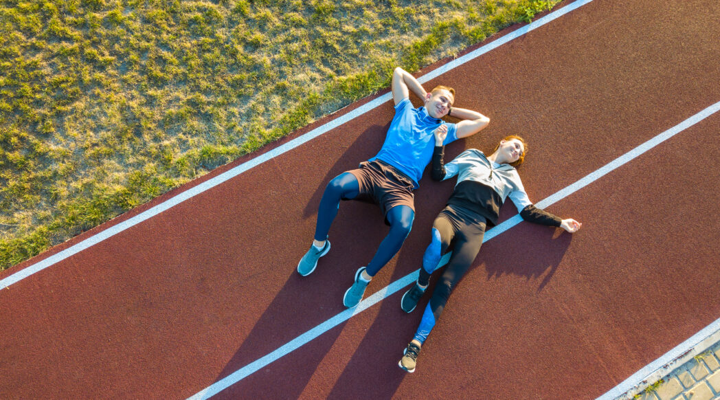 Two athletes rest on the running track during their taper