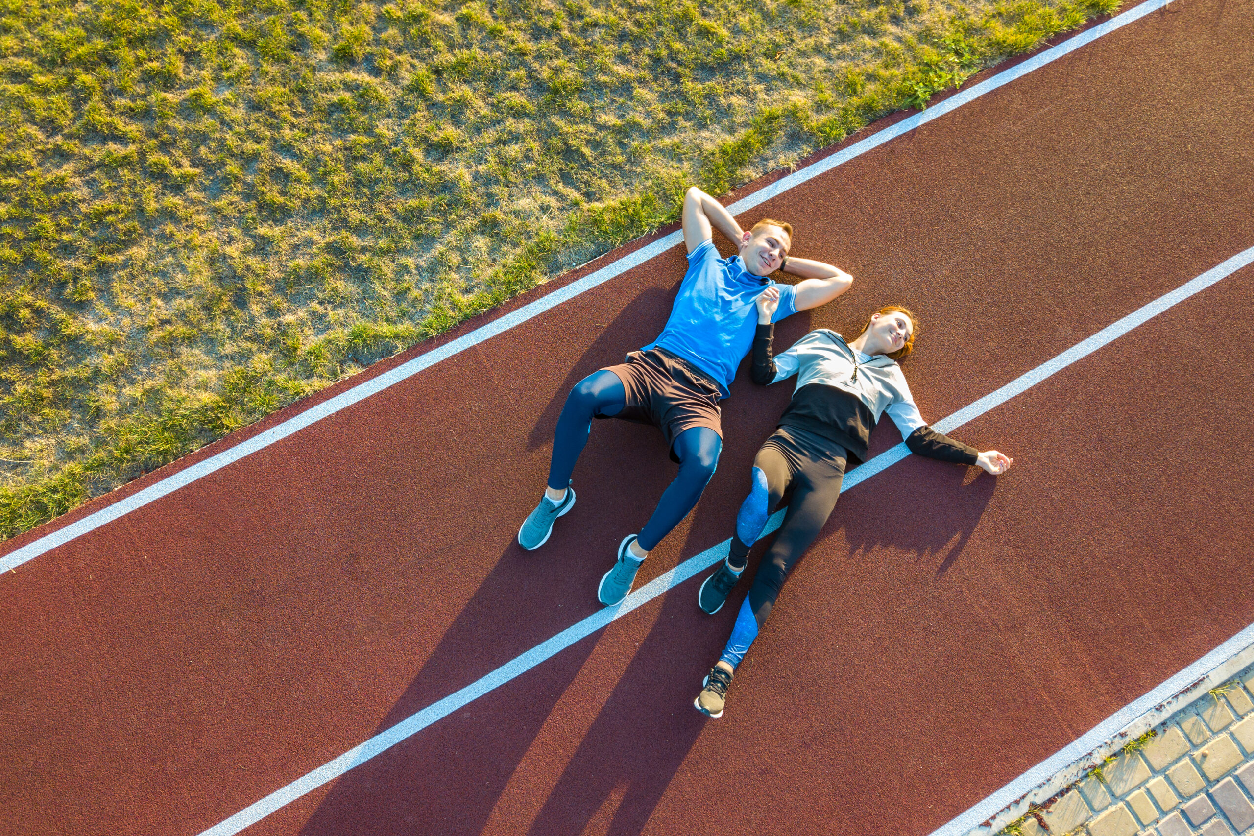 Two athletes rest on the running track during their taper