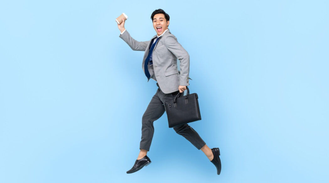 A young professional businessman with a smile runs with a suitcase and coffee.