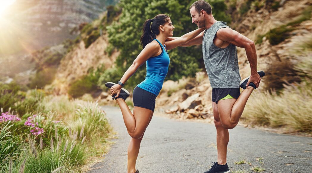 Two young runners, a man and a woman, stretch together before a run to minimize injury